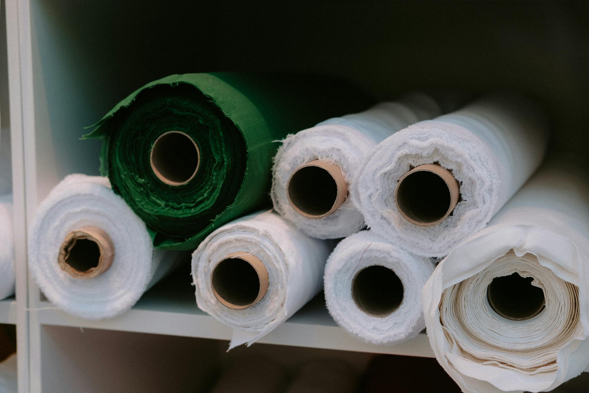 Close-up of rolls of fabric in various colors neatly arranged on a shelf in a storage area.