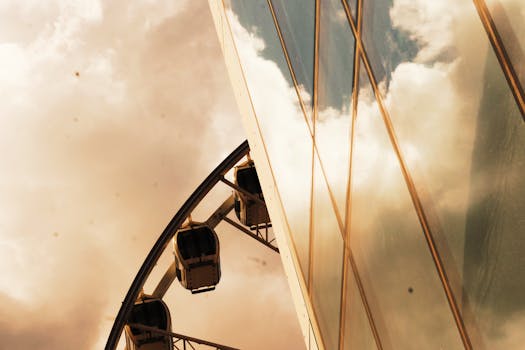 摩天轮在多云的天空下，映照在现代玻璃建筑中