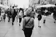 这张单色照片聚焦于一条繁忙的城市街道，从后方拍摄，画面中人们正在行走，焦点是一名女子