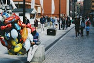 热闹的户外市场街道上，五颜六色的气球摆放着，行人熙熙攘攘