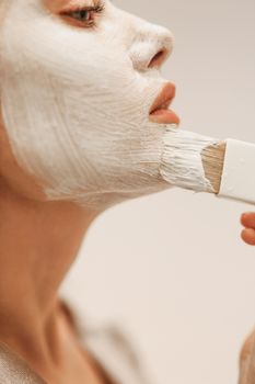 Detailed shot of a woman applying a white face mask with a brush, highlighting skincare routine.
