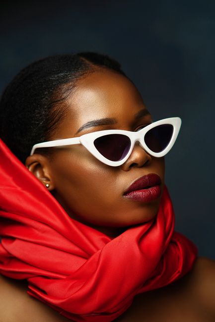 Stylish portrait of a woman wearing a red scarf and white sunglasses, conveying elegance and fashion.