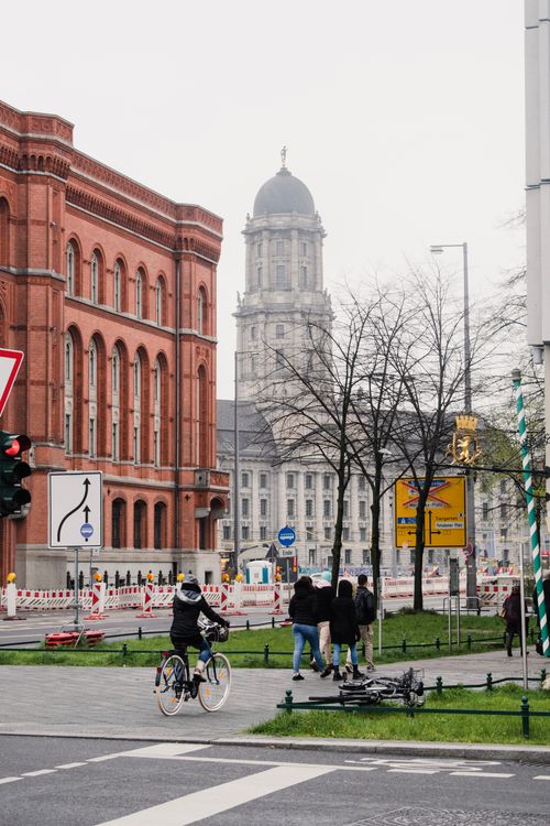 Free A cyclist rides through a busy street in Berlin with historic buildings and autumn trees in the background. Stock Photo