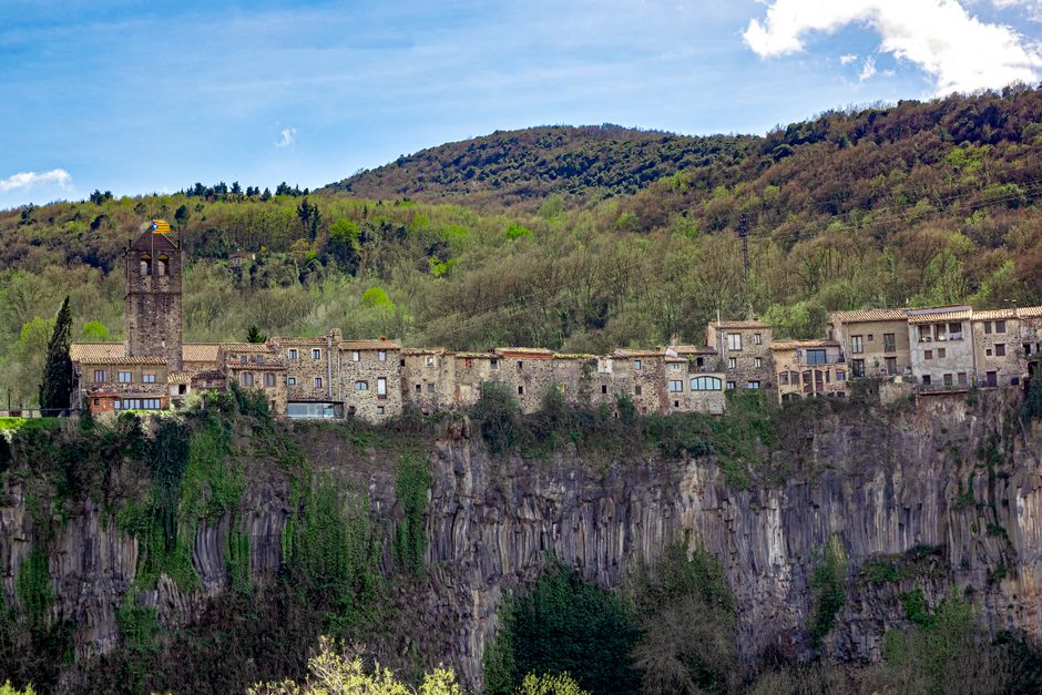 Picturesque village of Castellfollit de la Roca atop a basalt cliff with lush greenery.