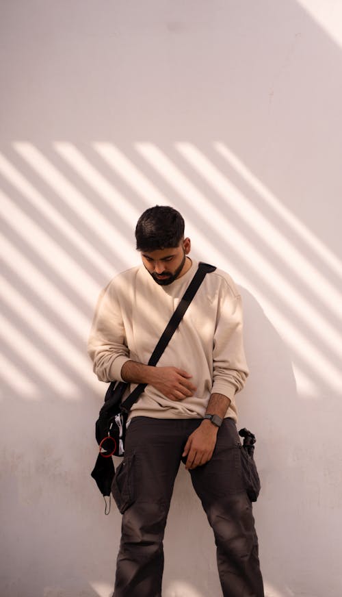 A Man in Beige Sweater Looking Down while Leaning on the Wall