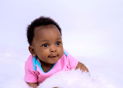 Cute African American baby girl in a pink outfit during a studio shoot, smiling warmly.