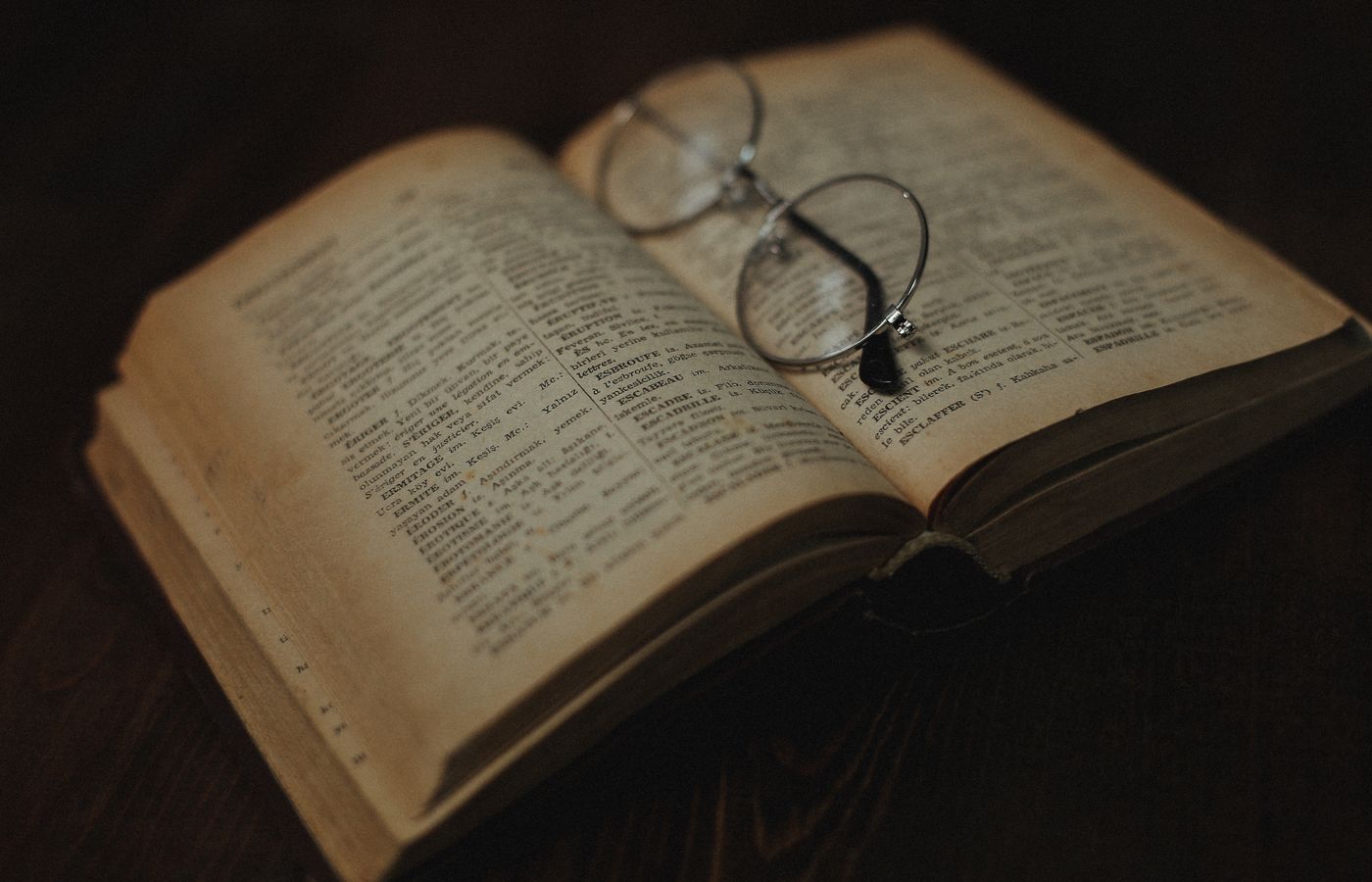 An antique book opened with eyeglasses resting on its pages. Aesthetic, warm lighting.