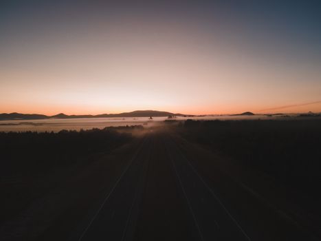 A breathtaking view of a road disappearing into the misty countryside at twilight, under a serene sky.