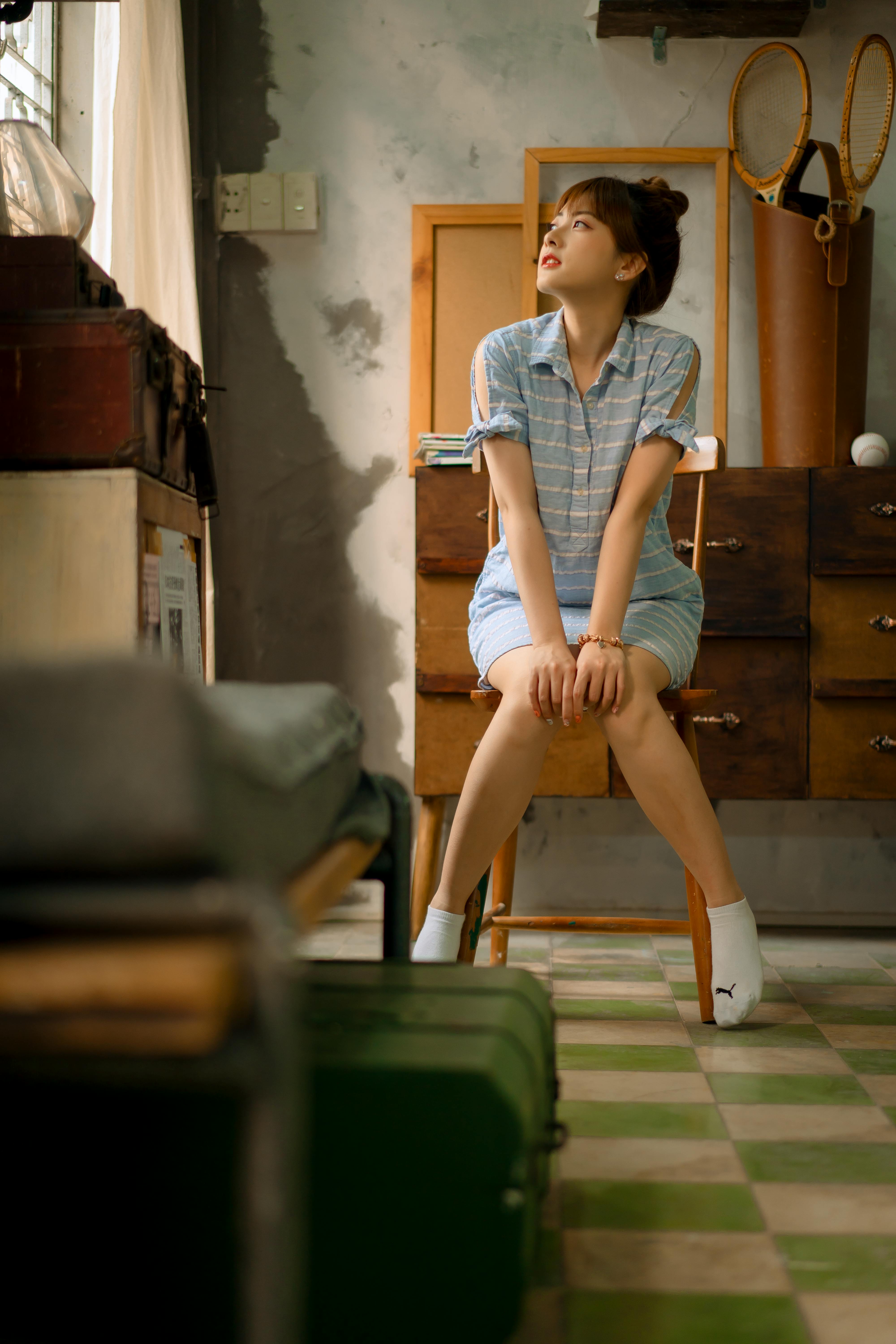 Asian woman in casual attire sits thoughtfully in a vintage styled room.
