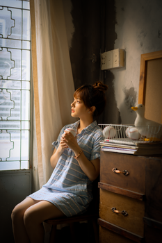 Asian woman sits by the window with a thoughtful expression.