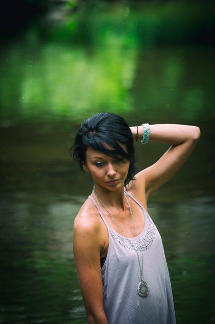 Elegant young woman in an outdoor photoshoot by a tranquil lake, showcasing fashion and nature.