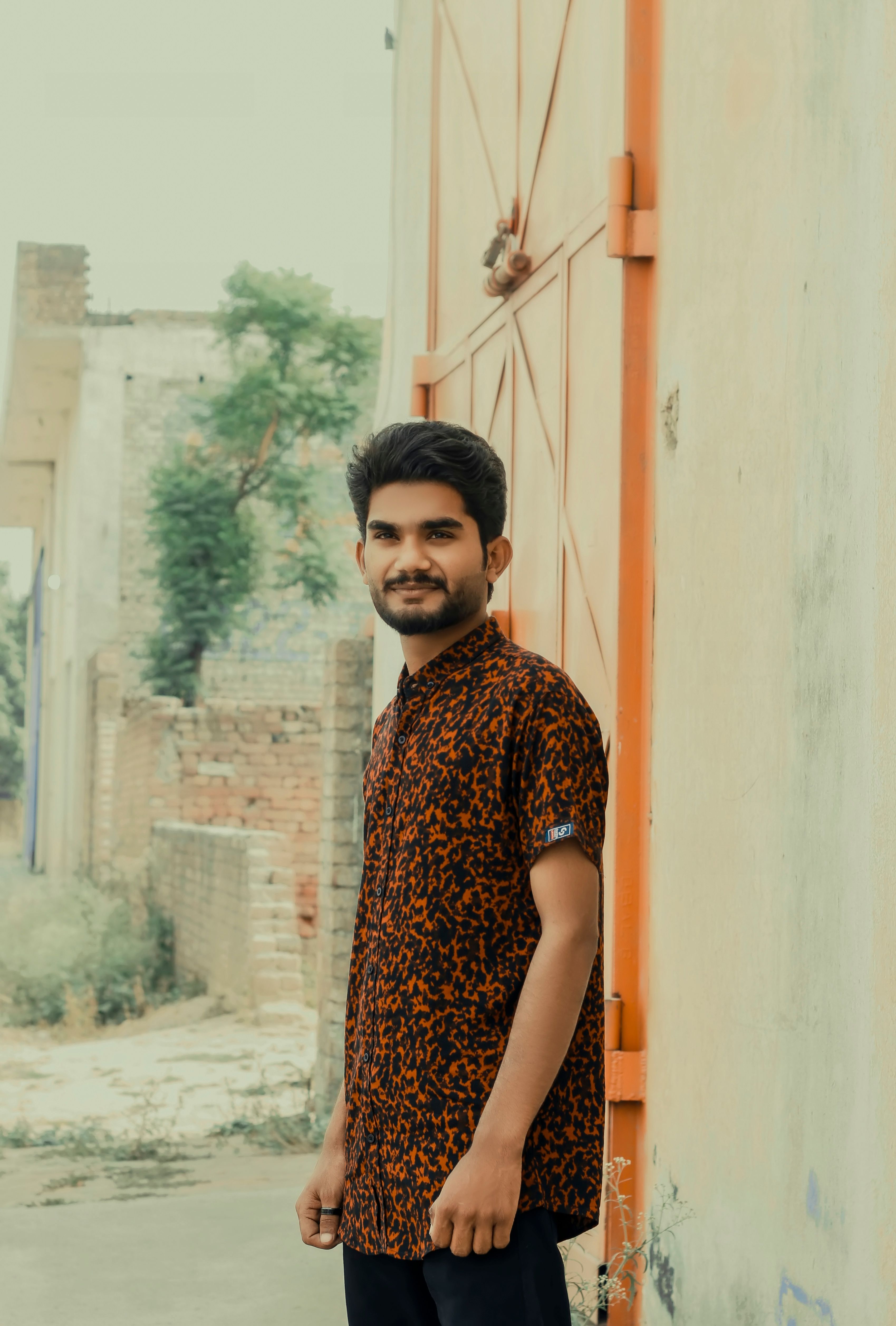 Portrait of a young man standing outside near a brick wall, exuding confidence and style.