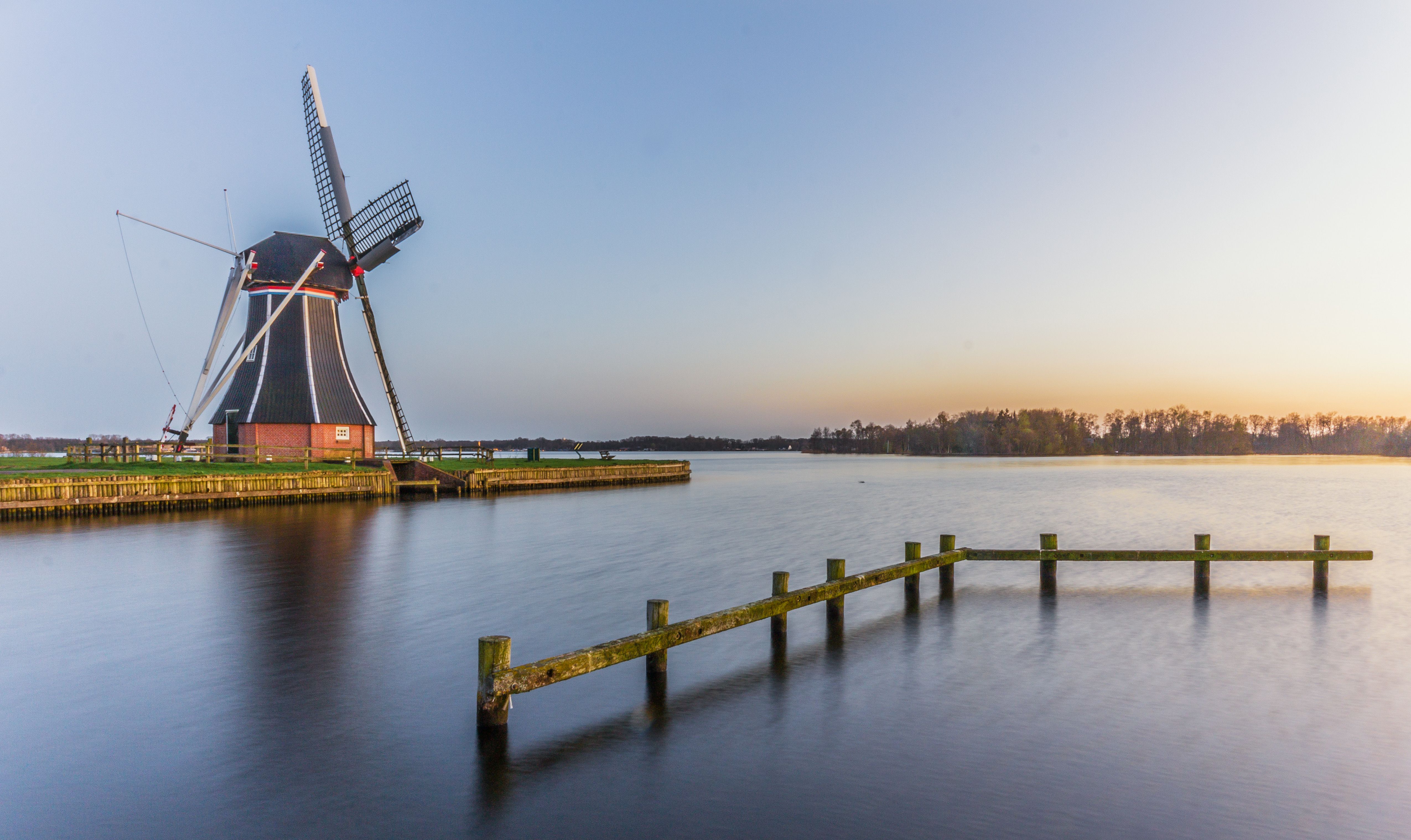 A picturesque windmill by a serene lake in Paterswolde, Netherlands during sunset.