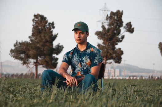 Man in Blue and White Floral Shirt and Blue Denim Jeans Sitting on Green Grass during