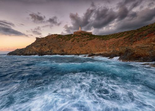 Free Breathtaking view of El Marsa coast with waves crashing against rocks at sunset, featuring a lighthouse. Stock Photo