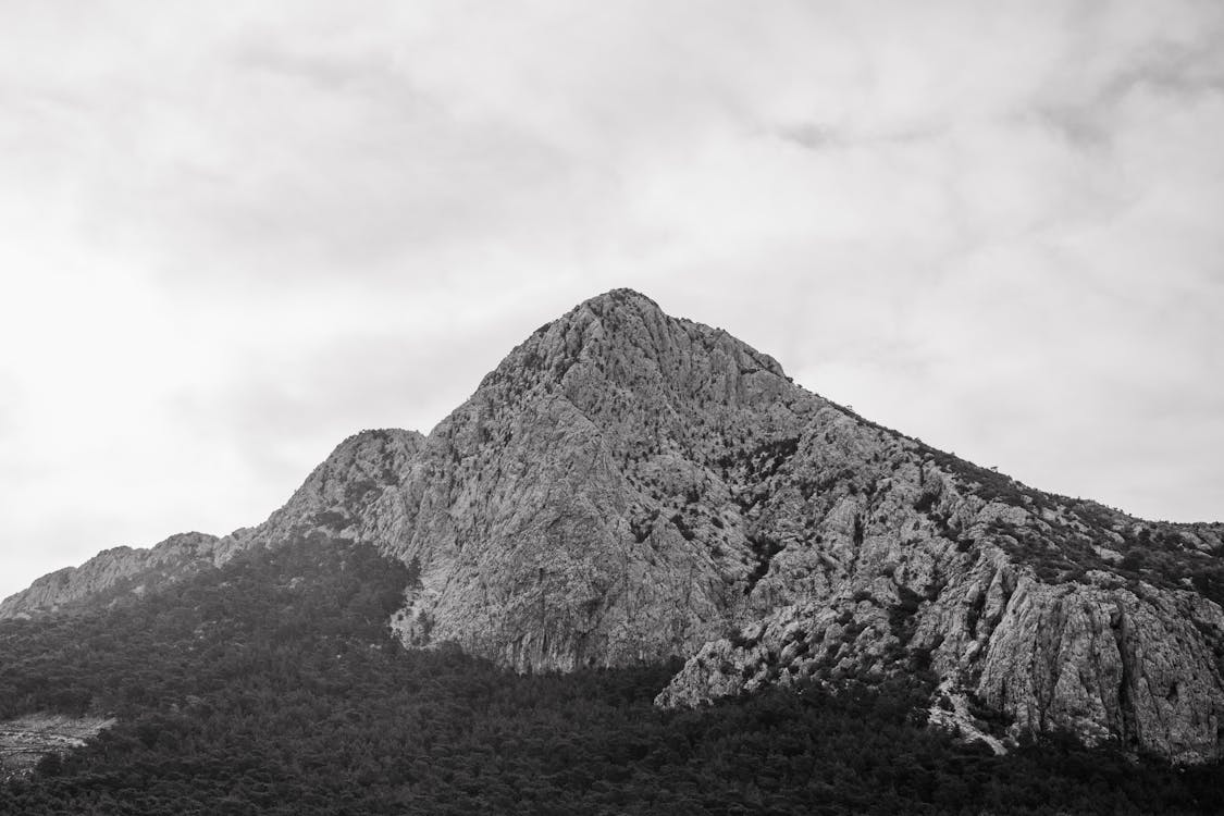 Grayscale Photo of Mountain Under Cloudy Sky