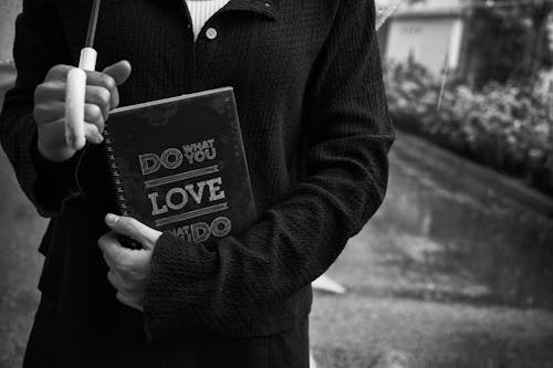 Grayscale Photo of a Person Holding Notebook