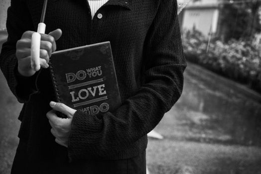 Close-up black and white image of a person holding a motivational notebook outdoors.