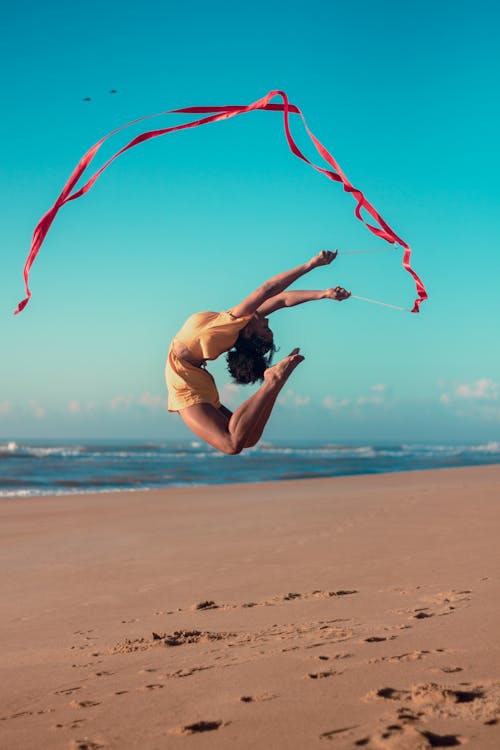 Free Woman Performing Extreme Gymnastic Exercise with Ribbon on Beach Stock Photo