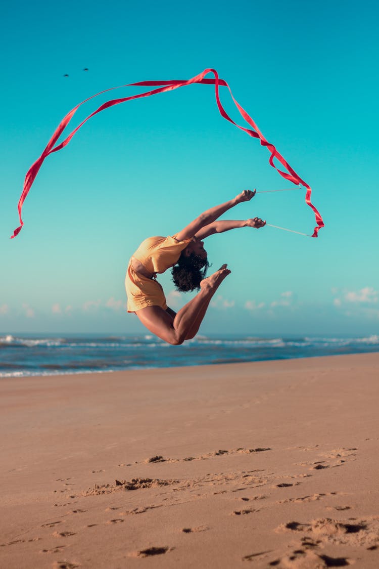 Woman Performing Extreme Gymnastic Exercise With Ribbon On Beach