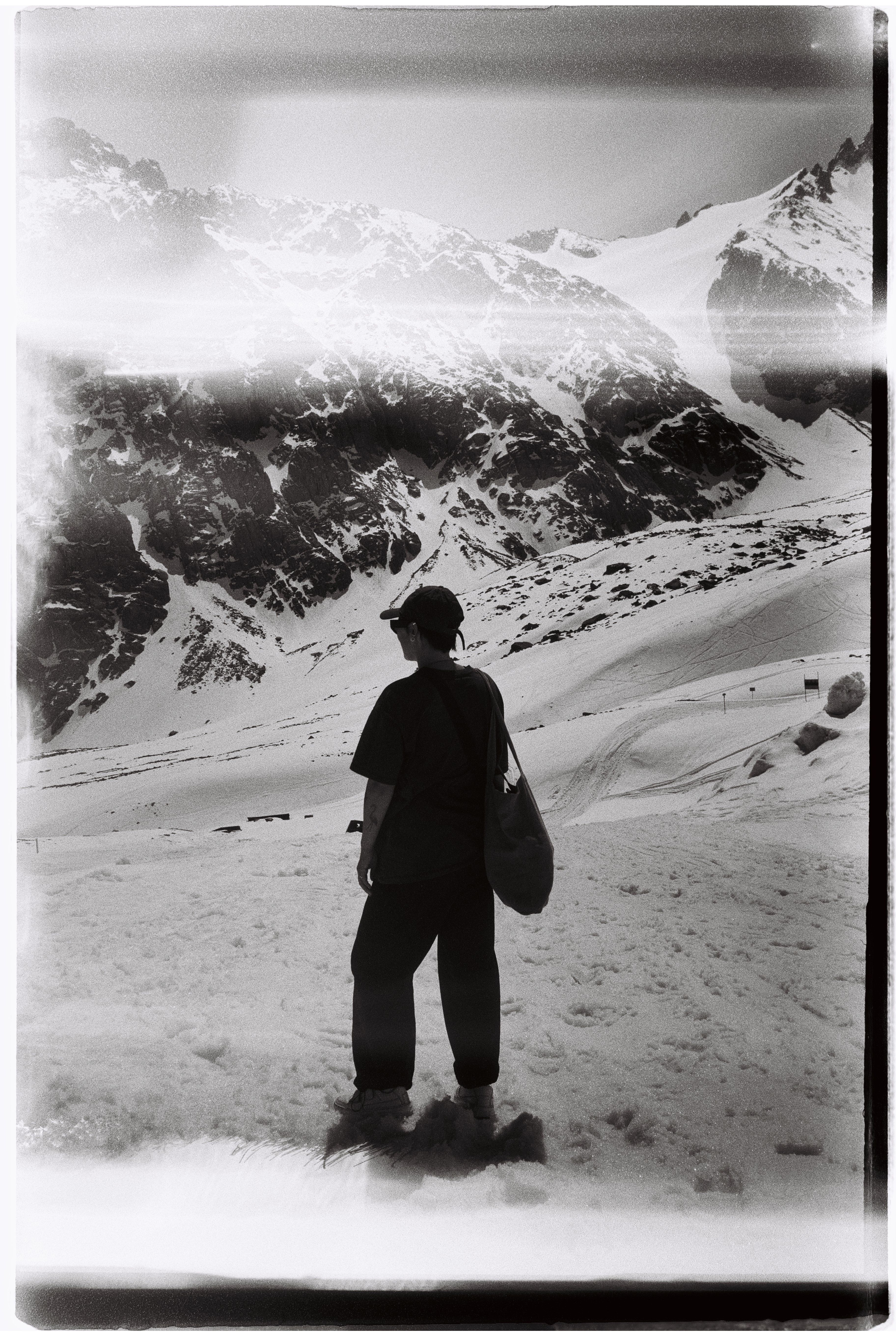 Black and white image of a person standing, gazing at the snowy mountains in Kazakhstan.