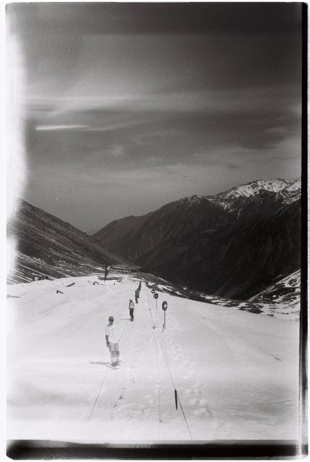 Black and white image of skiers on a serene, snow-covered mountain slope in Almaty, Kazakhstan.