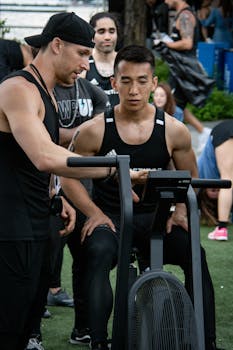 Asian man on stationary bike during an outdoor fitness session with a trainer.
