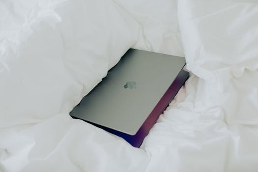 A gray laptop nestled in white bedding, depicting a relaxed and minimalist work-from-home setting.