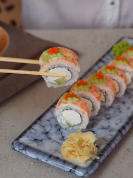 Vertical shot of sushi rolls with chopsticks, featuring caviar and ginger garnish.