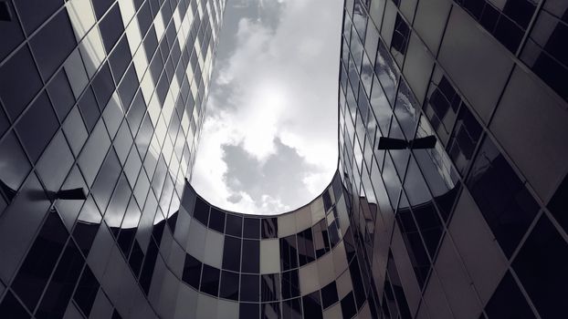 Curved modern glass building in Moscow with striking reflections against a cloudy sky.