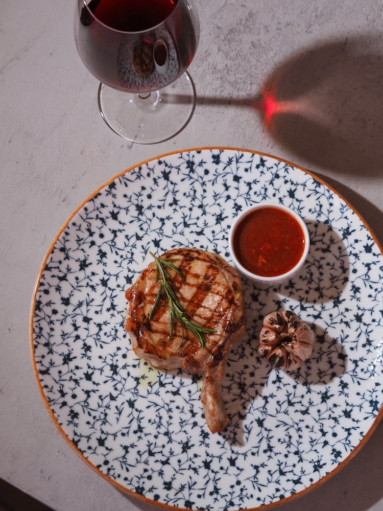 A Grilled Steak Topped With Rosemary With Garlic And Red Sauce On Plate