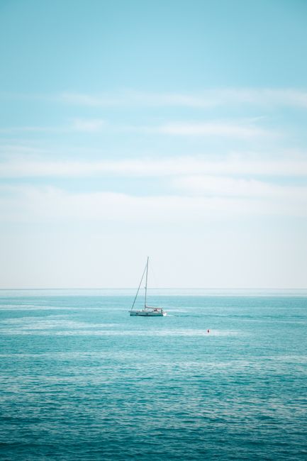 Peaceful sailing boat on the turquoise waters of Liguria, Italy under a bright blue sky.