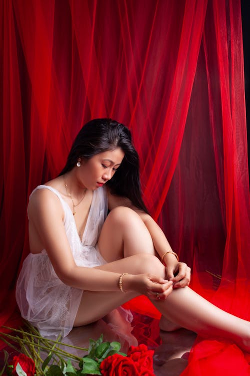 A Woman in White Lingerie Sitting Beside red Curtains