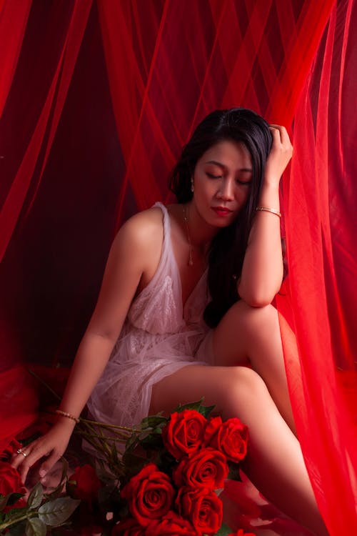 Brunette Woman in White Strap Dress Posing with a Bouquet of Red Roses