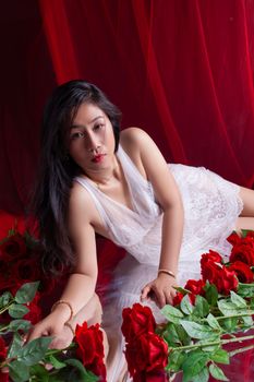 Beautiful Asian woman in white lace, surrounded by vibrant red roses, exudes elegance and sensuality.