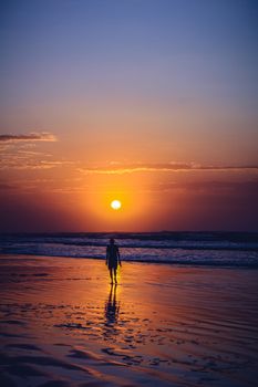 A solitary silhouette standing on a beach as the sun sets, casting vibrant hues across the sky.
