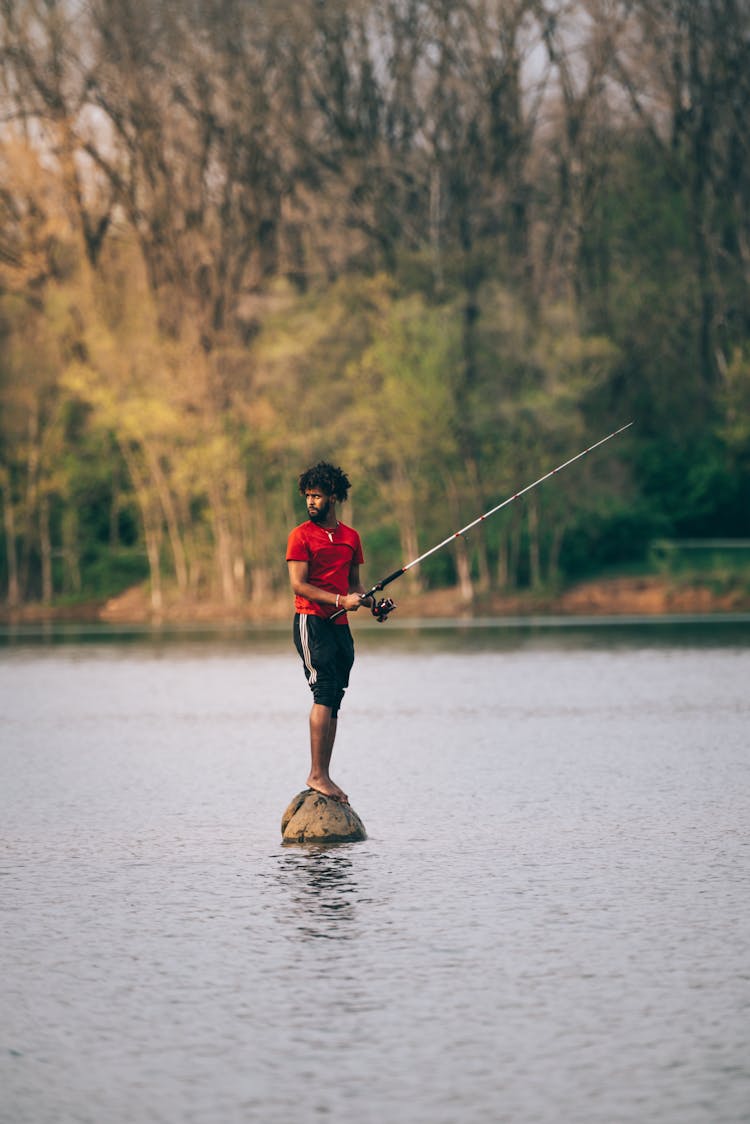 Man Standing On Rock In River With Fishing Rod