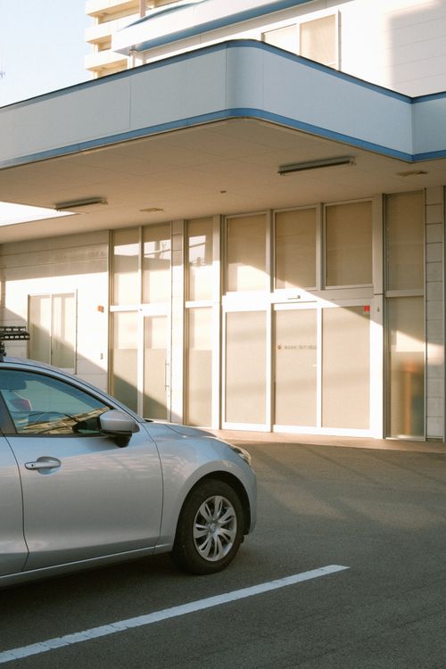 Free A silver car parked in an urban lot with a modern building facade in daylight. Stock Photo
