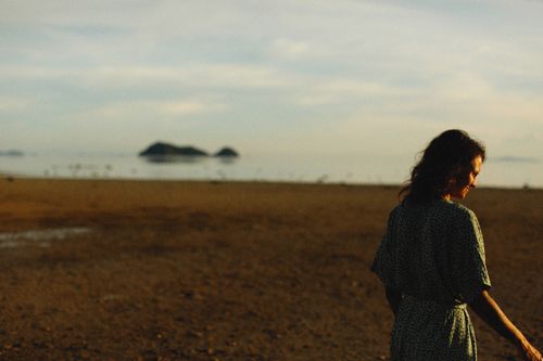 Free A woman walks along a serene beach during sunset with islands in the distance, capturing tranquility. Stock Photo
