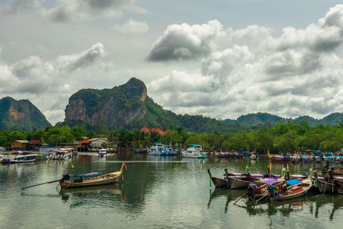 Free Boats moored in a calm river, surrounded by lush greenery and limestone cliffs under a cloudy sky. Stock Photo