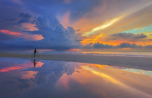 A Person Riding on a Bicycle on the Shore of a Beach Under Beautiful Sunset