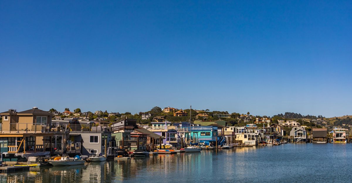 A picturesque marina with colorful boathouses and calm water under a bright blue sky, showcasing serene waterfront living.