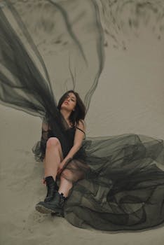 Striking image of a woman on a sandy beach wearing a flowing black tulle dress. Fashion and elegance in nature.