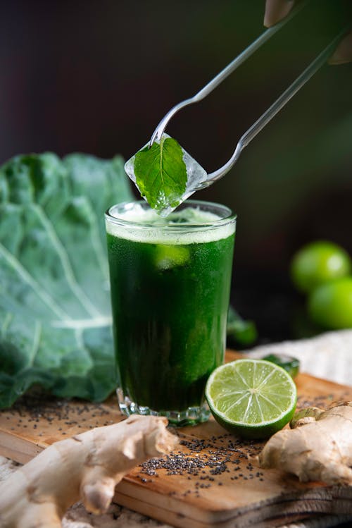 Person Putting an Ice cube with a Mint Leaf into a Green Juice