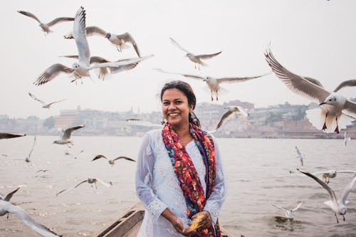 Woman in White Long Sleeve Dress Smiling Near Flying Birds 