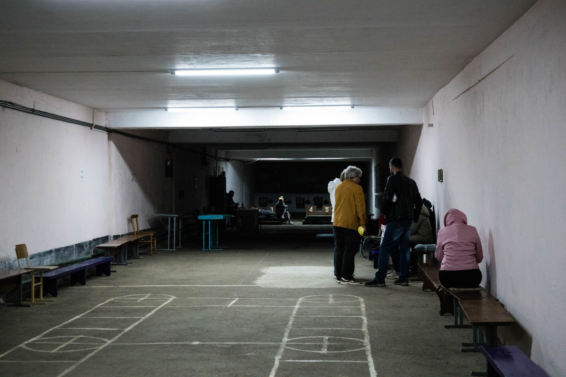 A group of people sitting and standing in an underground shelter with simple lighting and chalk drawings on the floor.