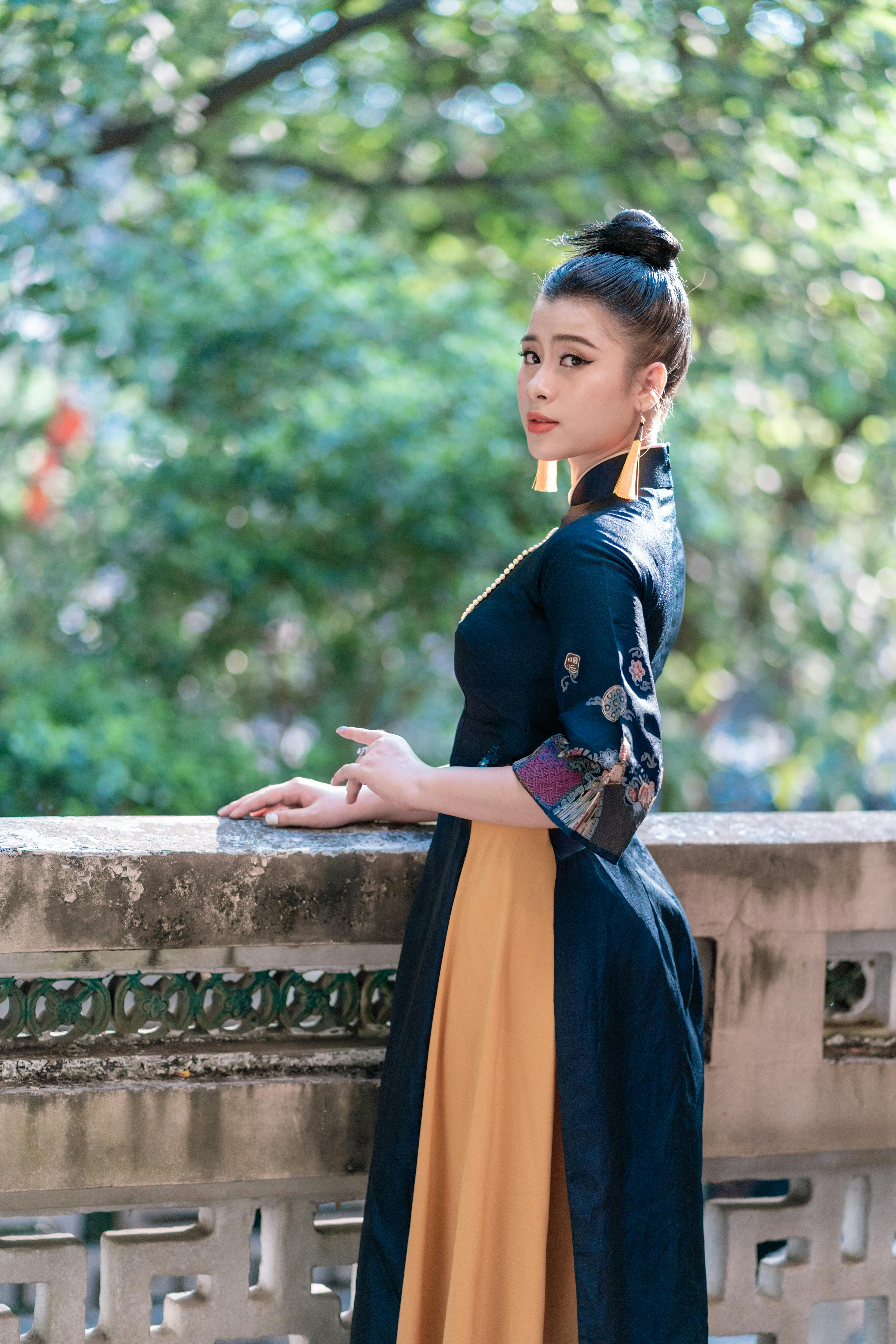 woman in traditional blue and yellow dress standing near concrete wall