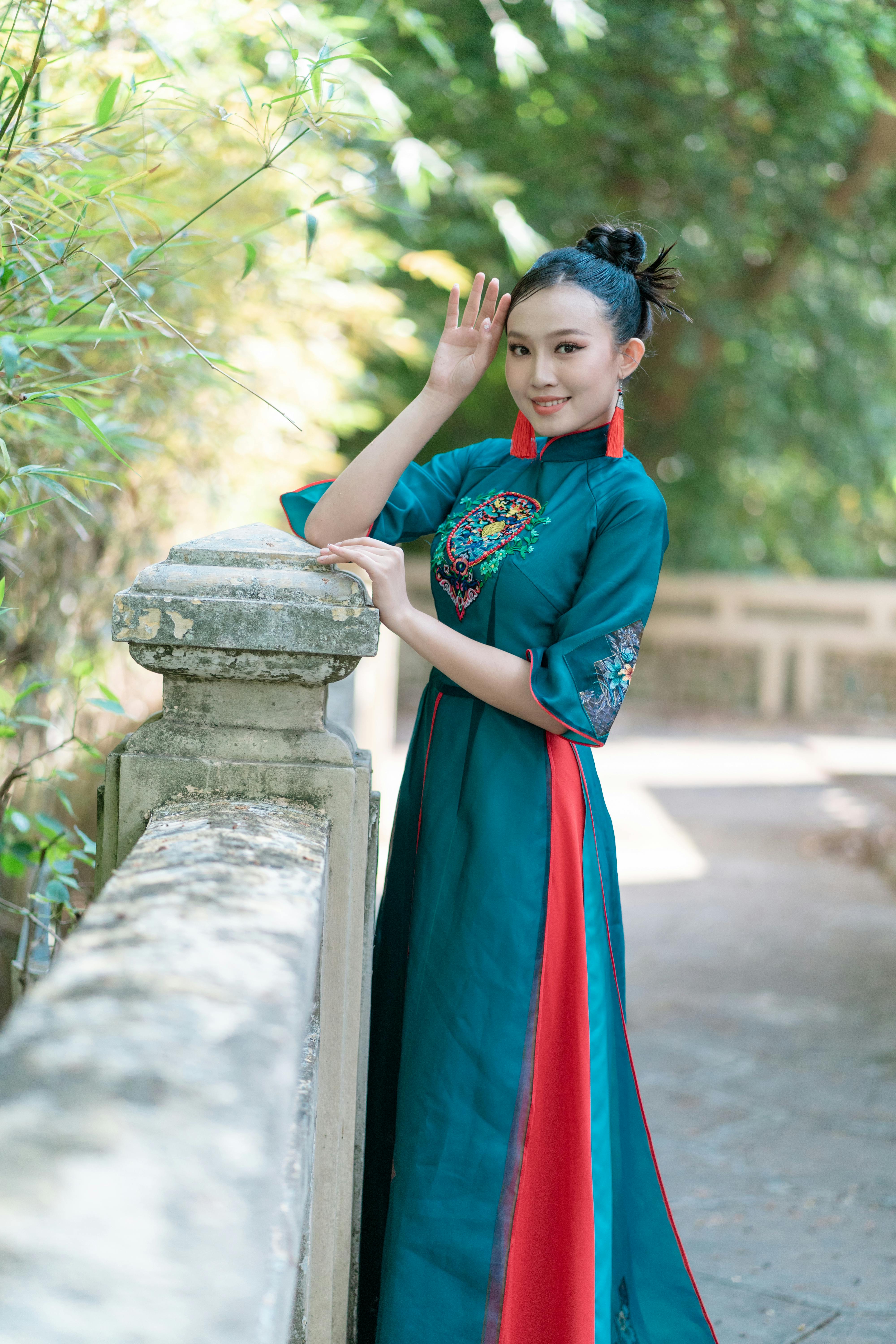 woman in blue and red traditional dress standing near concrete fence