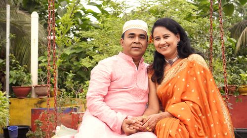 Free Smiling couple in traditional attire enjoying an outdoor setting filled with greenery. Stock Photo