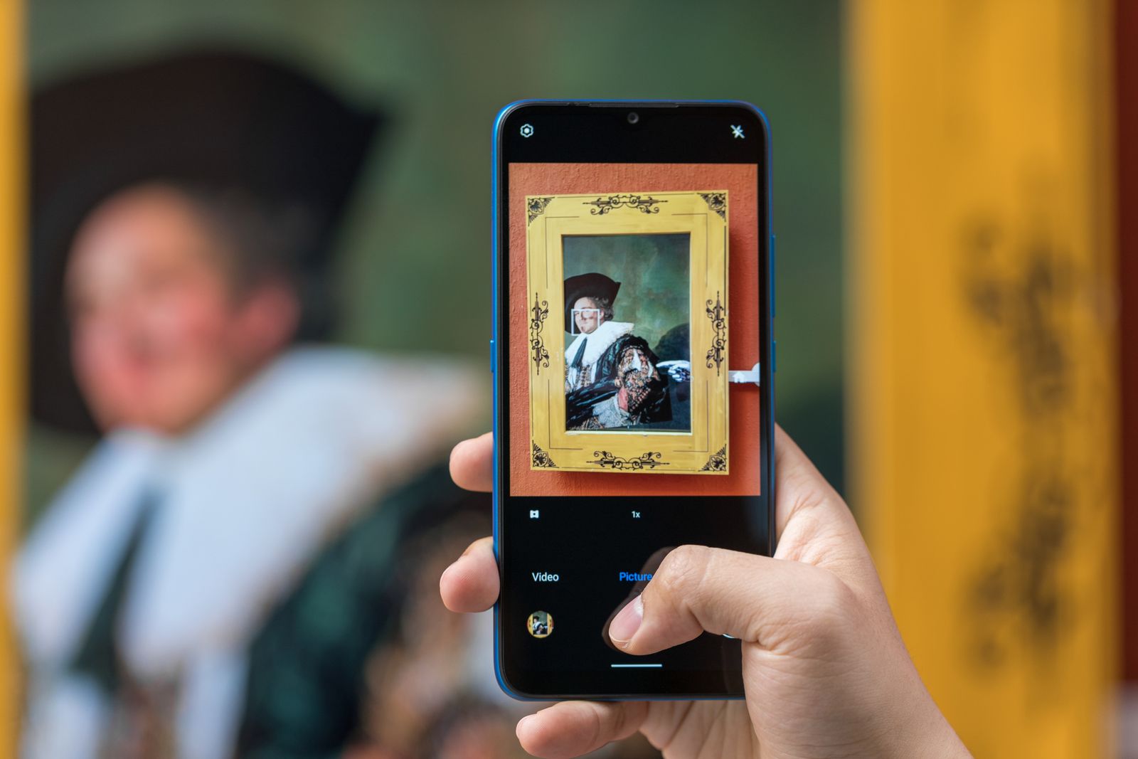A gallery visitor making a close smartphone photograph of a framed painting.